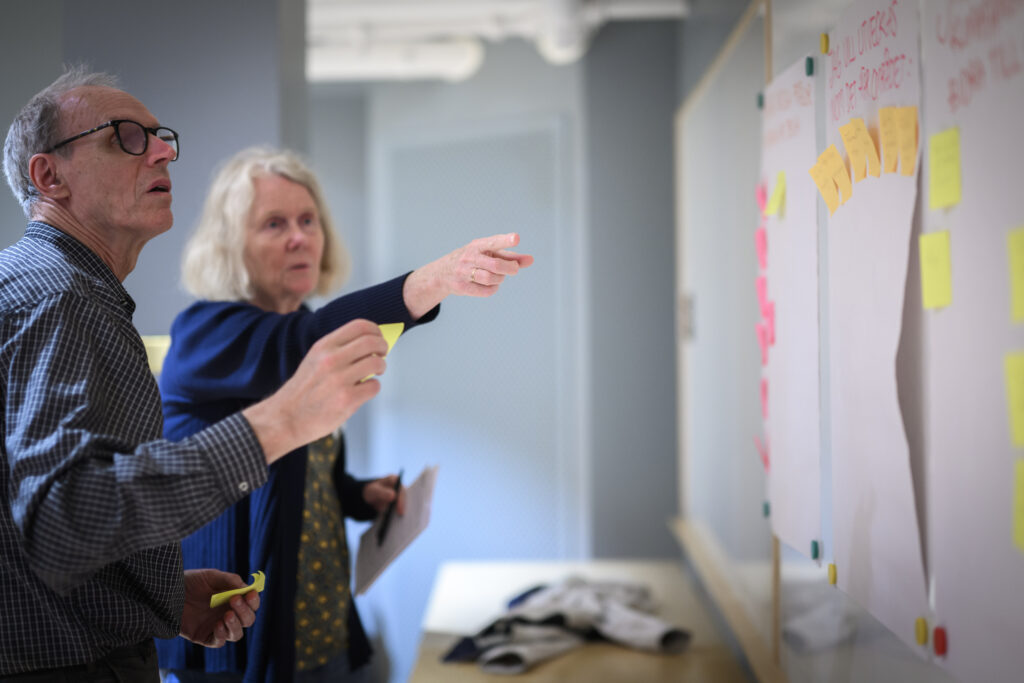 Två personer pekar på en whiteboardtavla där post-it-lappar är fästa.