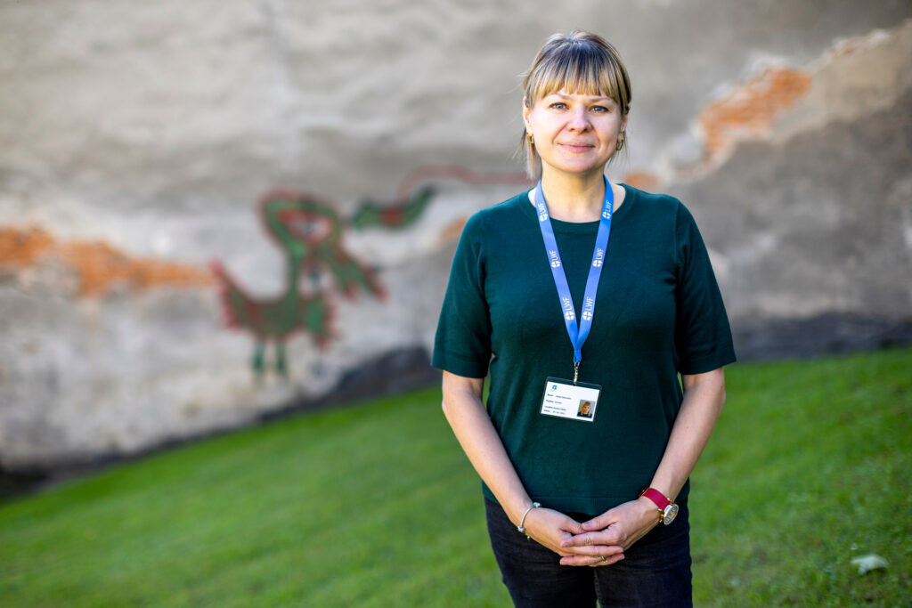 En kvinna i grön tröja står  på en gräsmatta framför en mur. 