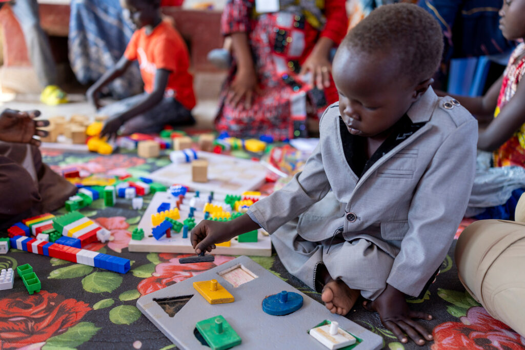 Ett barn sitter och pusslar på en matta.