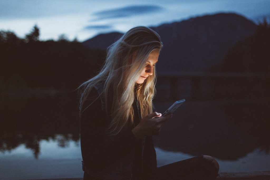 Kvinna läser på mobiltelefon utomhus på kvällen vid en sjö