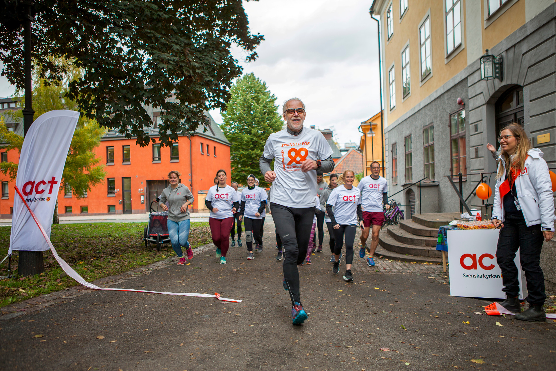 Grupp människor springer mot kameran. De bär tröjor med Act Svenska kyrkans logga på.