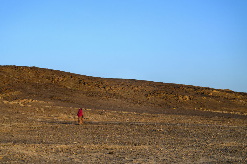 En kvinna står ensam långt borta i ett torrt och ödsligt ökenlandskap.
