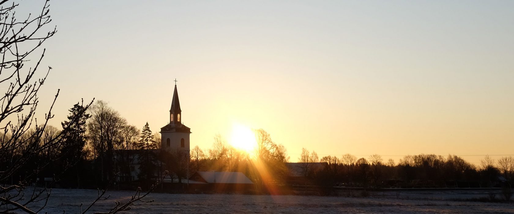 Solen står lågt över Floby kyrka och lyser över den frostiga marken
