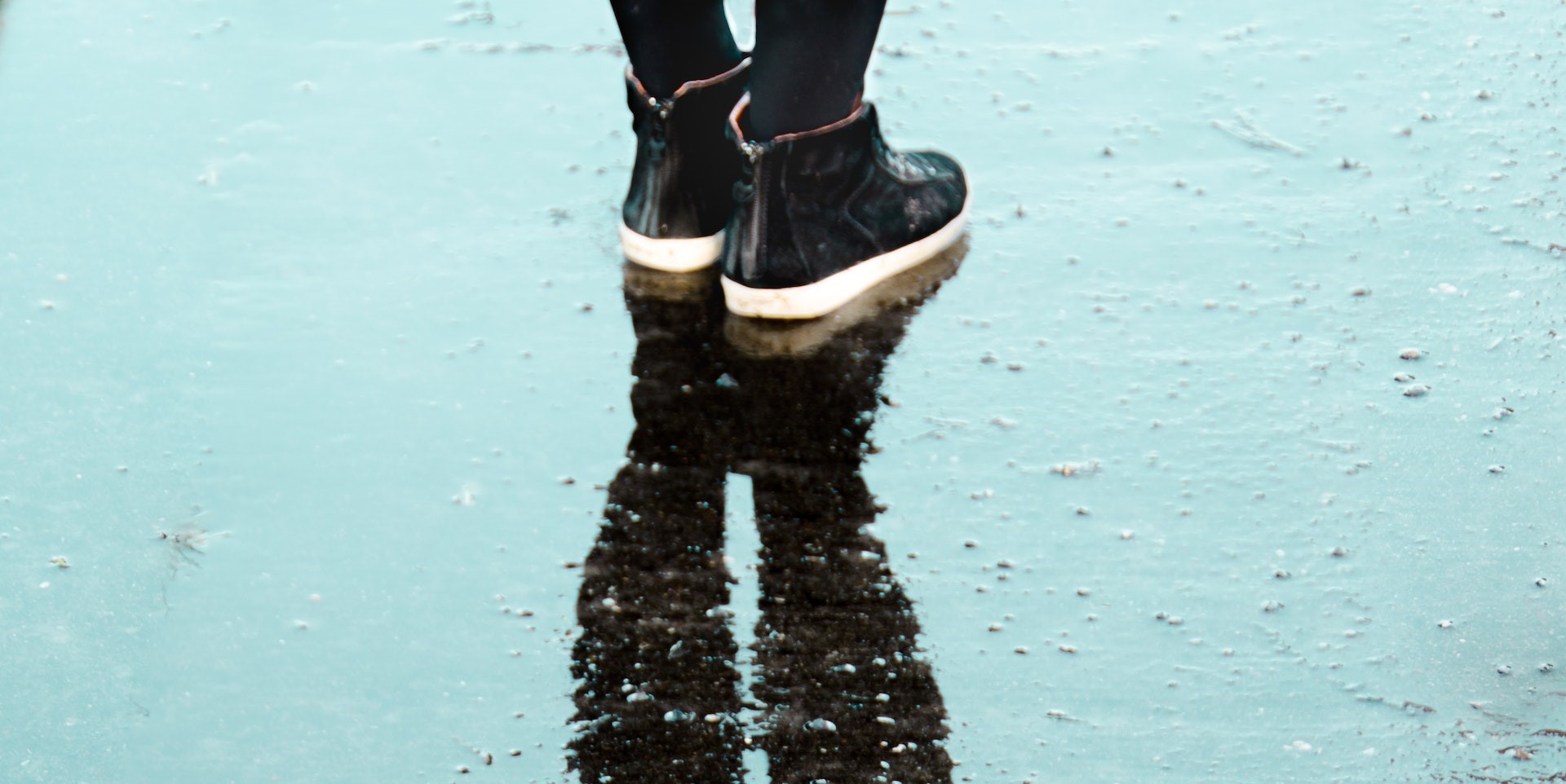 Nederdelen av ett par ben i låga kängor, på en regnvåt gata.