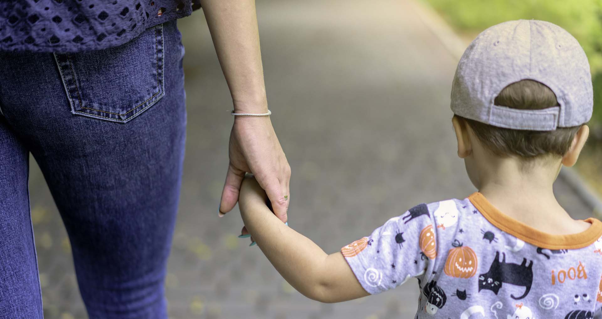 Ryggtavlorna av en mamma och en liten pojke som går gatan fram och håller varandra i handen.