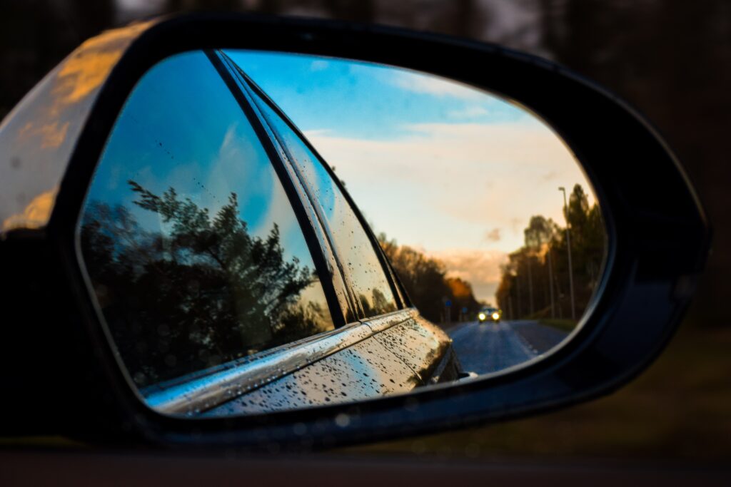 En sidobackspegel speglar en del av bilen, en landsväg och skog. 