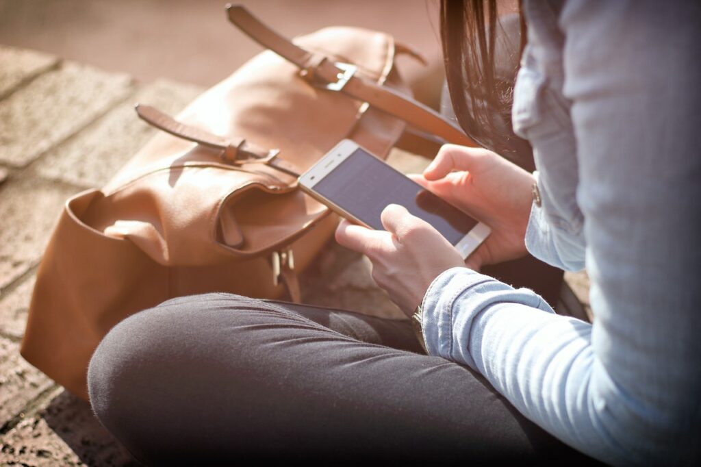 En kvinna sitter på marken och tittar i sin mobiltelefon.